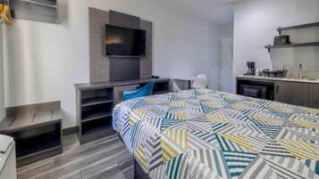 Ein modernes Hotelzimmer mit Bett, Schreibtisch mit Stuhl, einem wandmontierten Flachbildfernseher und einer Küchenzeile.