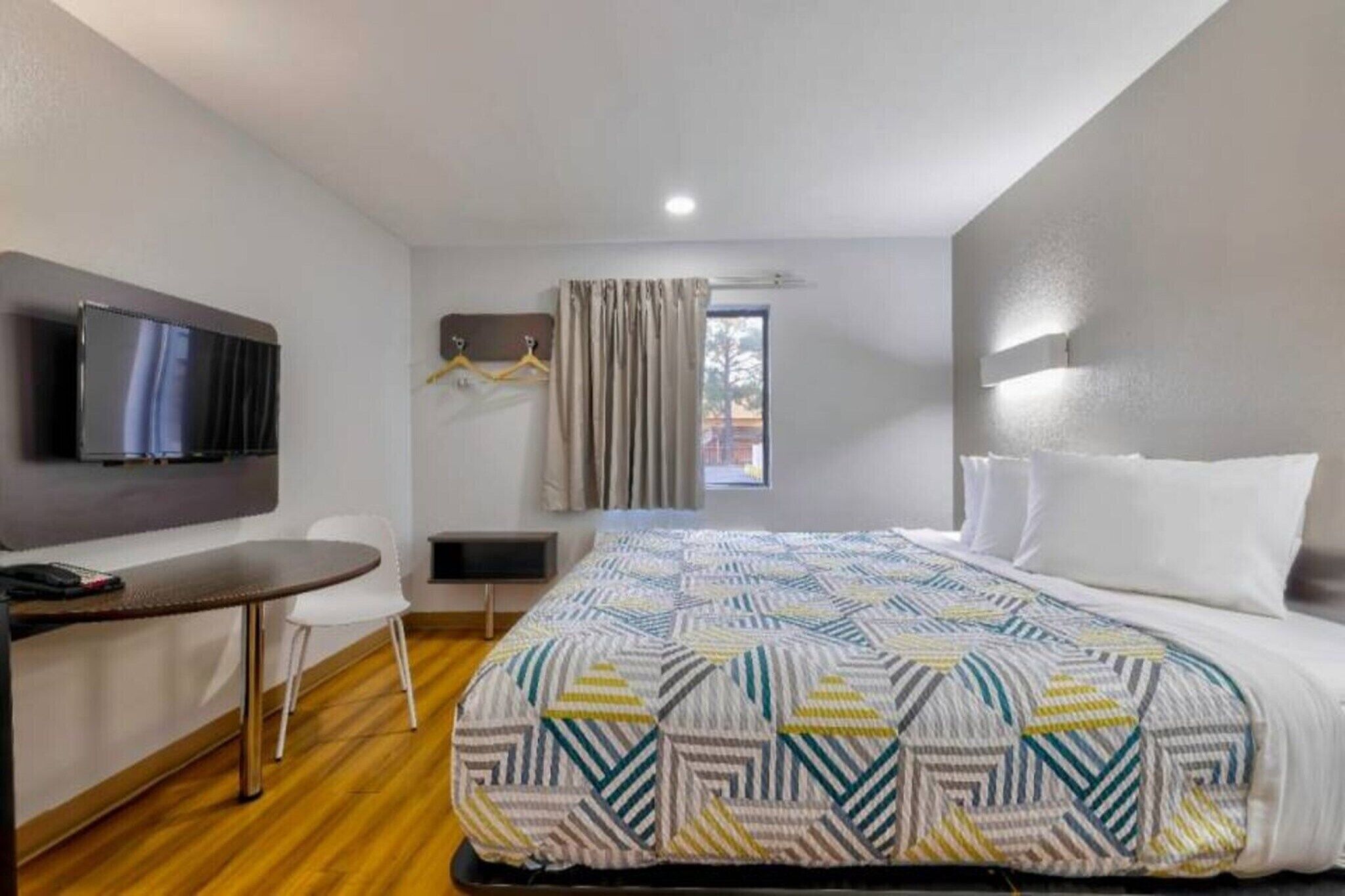 A hotel room with a bed, a desk, a chair, a TV, and a window with curtains.