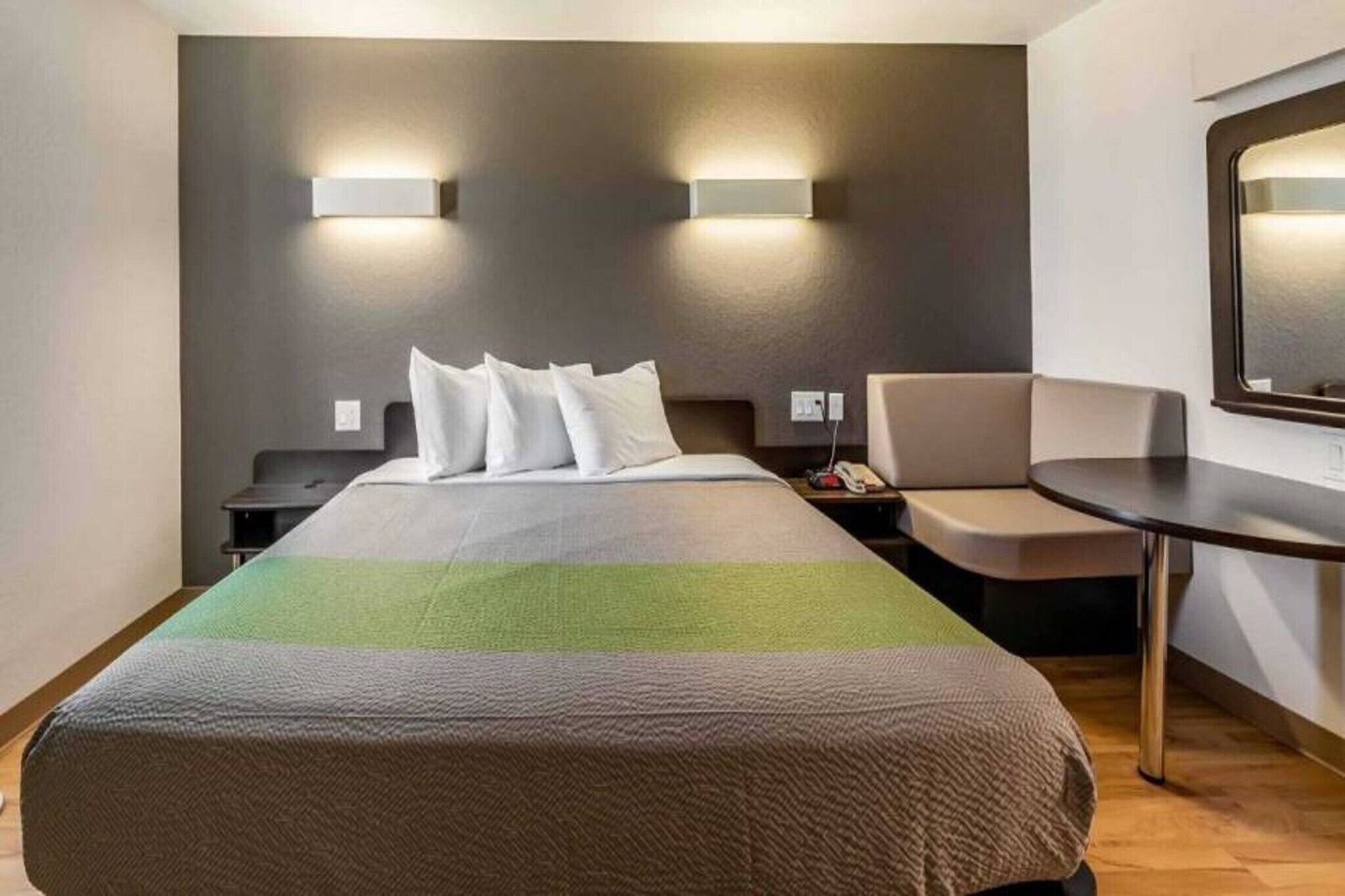 A hotel room with a bed, bedside tables, a chair, a small table, and wall-mounted lights.