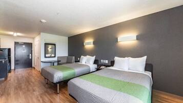 A hotel room with two beds, a desk, a mirror, and a kitchenette.