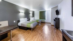 A hotel room with two beds, a desk, a TV, and a window with curtains.