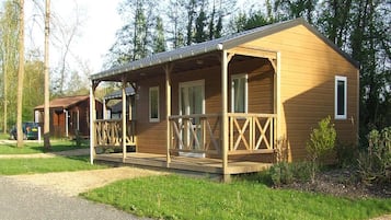 A wooden cabin with a porch, a car parked nearby, and a gravel path leading to it.
