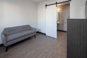 Une pièce avec un canapé gris, une porte coulissante donnant sur une salle de bain et un meuble en bois.