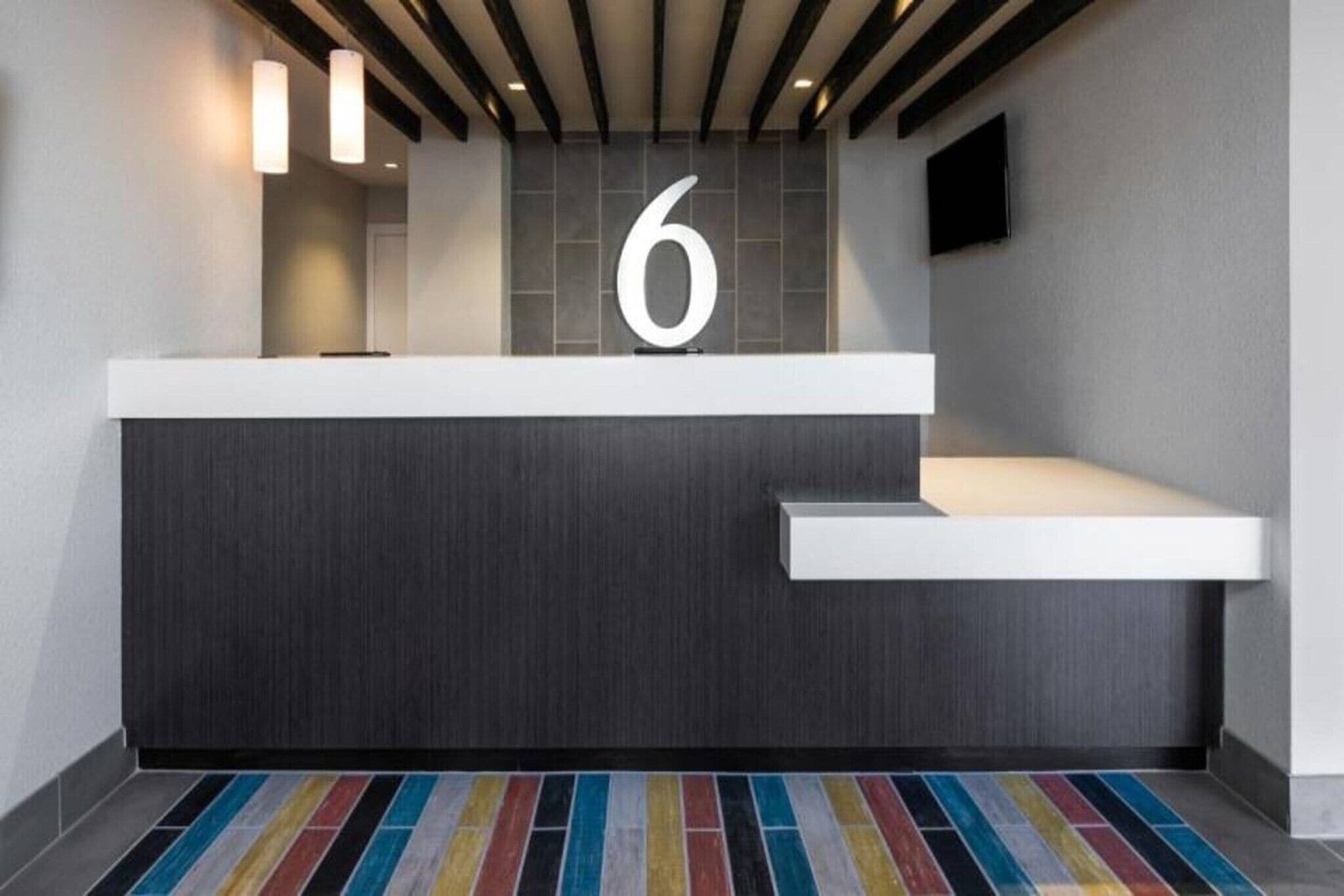 Un mostrador de recepción moderno con un gran número '6' encima, una encimera blanca y una alfombra a rayas coloridas.