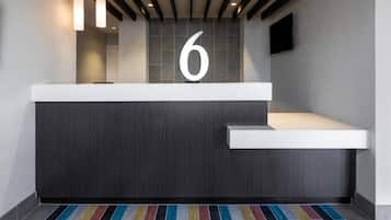 Un mostrador de recepción moderno con un gran número '6' encima, una encimera blanca y una alfombra a rayas coloridas.