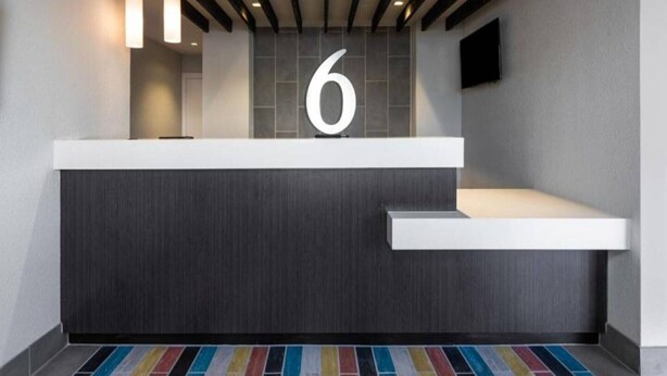 A modern reception desk with a large number '6' above it, a white counter, and a colorful striped carpet.