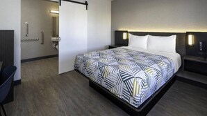 A hotel room with a bed, a desk, a chair, a nightstand, and a bathroom door.