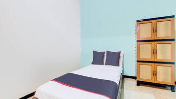 A single bed with a white and red bedspread, two pillows, and a wooden wardrobe with multiple compartments.