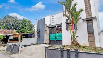 A modern building with a flat roof, a green gate, and a palm tree.