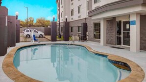 A swimming pool with a stone border, a gated entrance, and a building with a sign indicating a fitness center. - 2 Queen Beds | Mobil Access Tub Nsmk Micfridg (Balch Springs)
