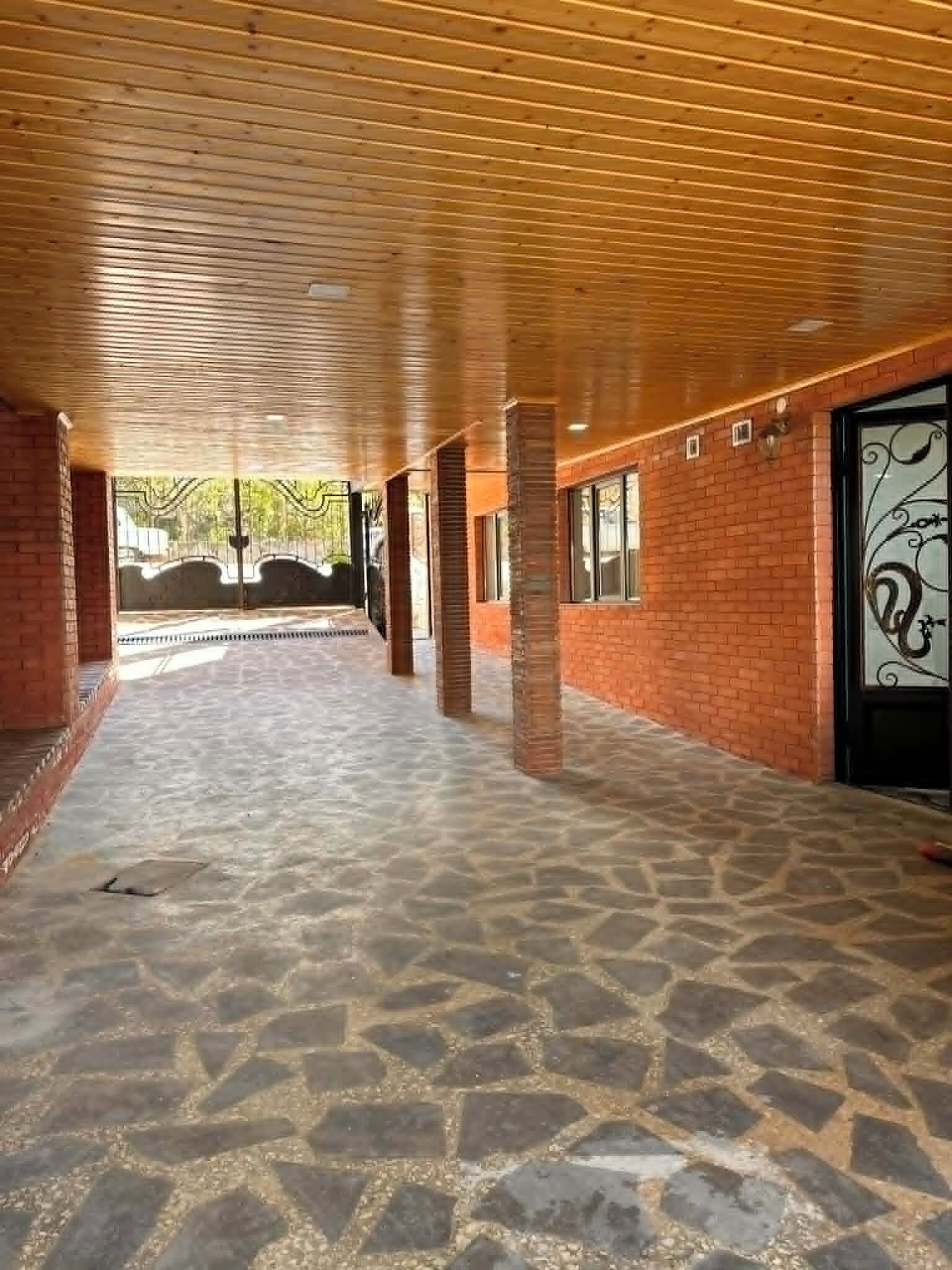 Un espacio al aire libre cubierto, con suelo de piedra estampada, paredes de ladrillo y vigas de madera en el techo.
