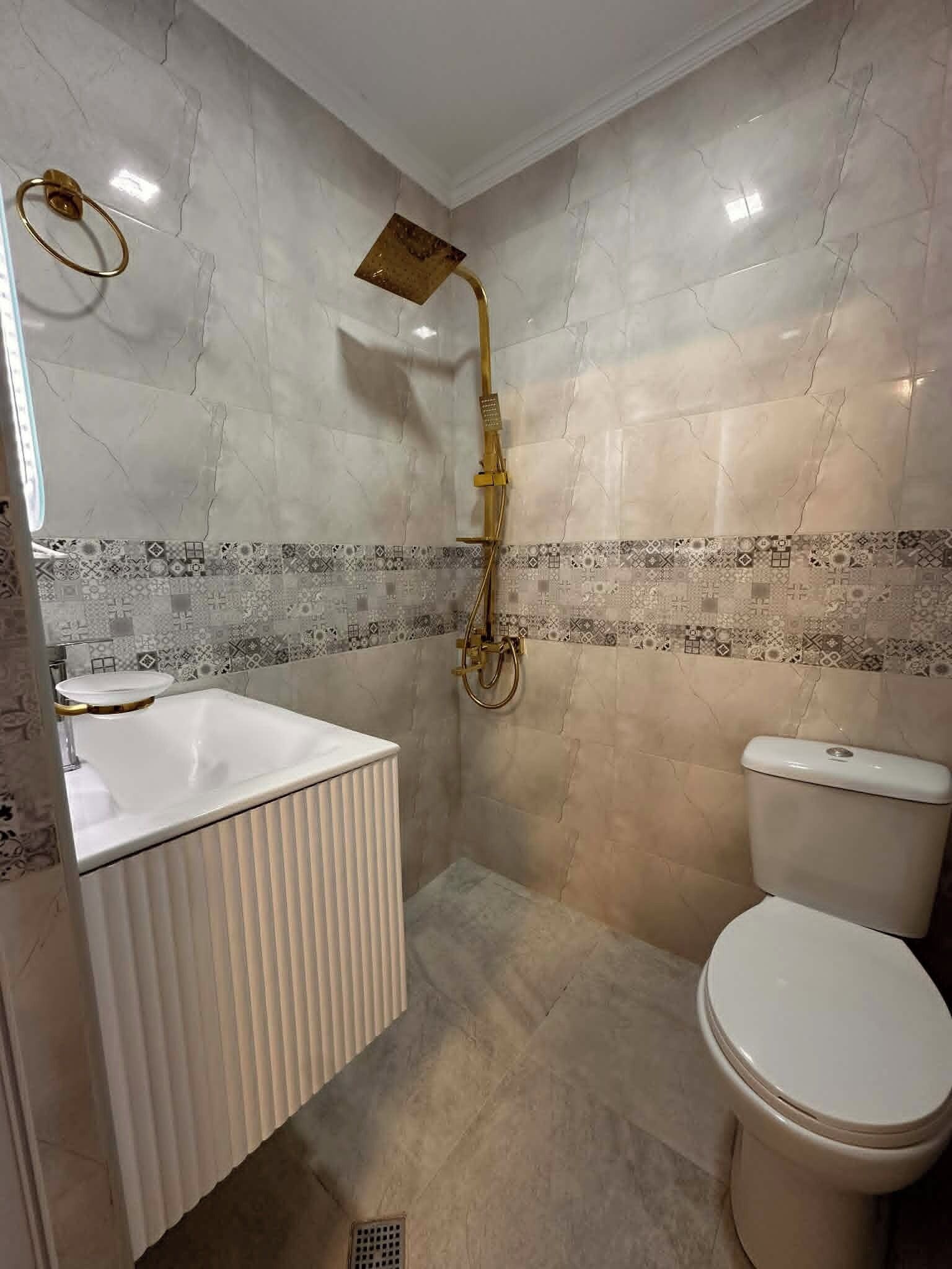 A bathroom with a white sink, a toilet, and a shower with a gold fixture.
