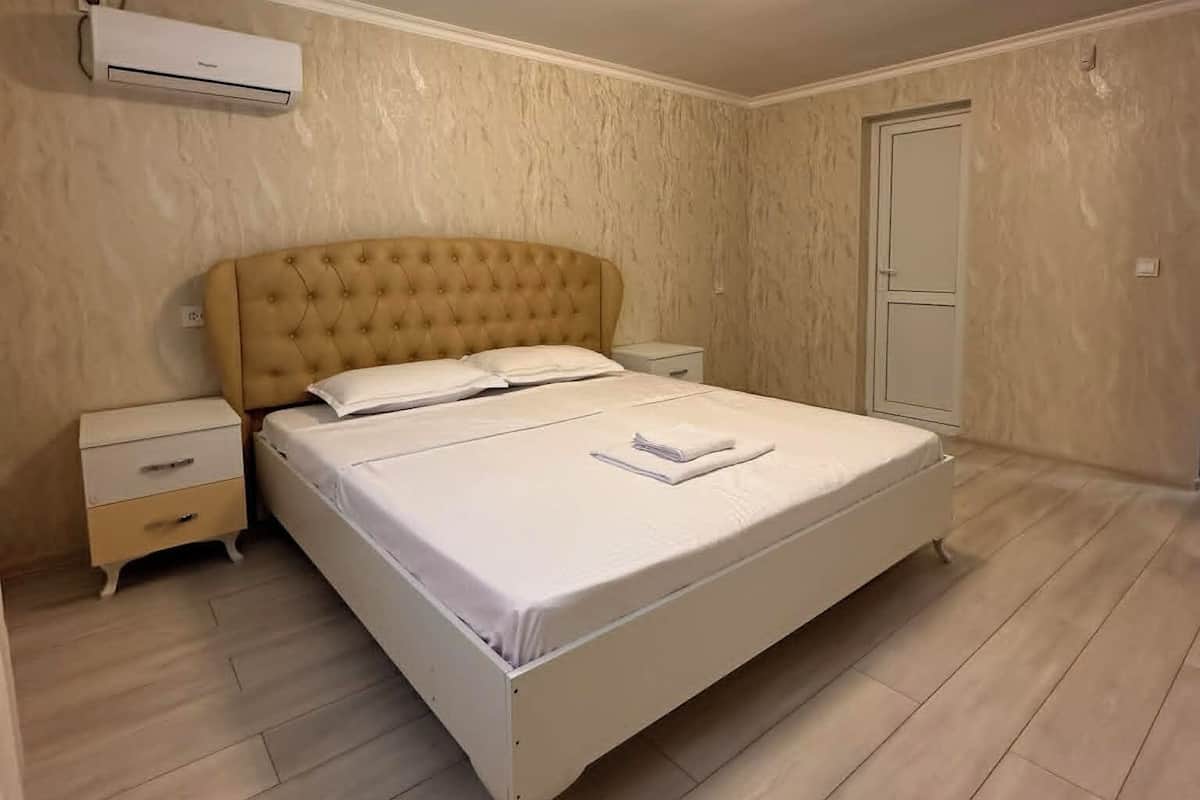 A bedroom with a bed, nightstands, an air conditioning unit, and a door.