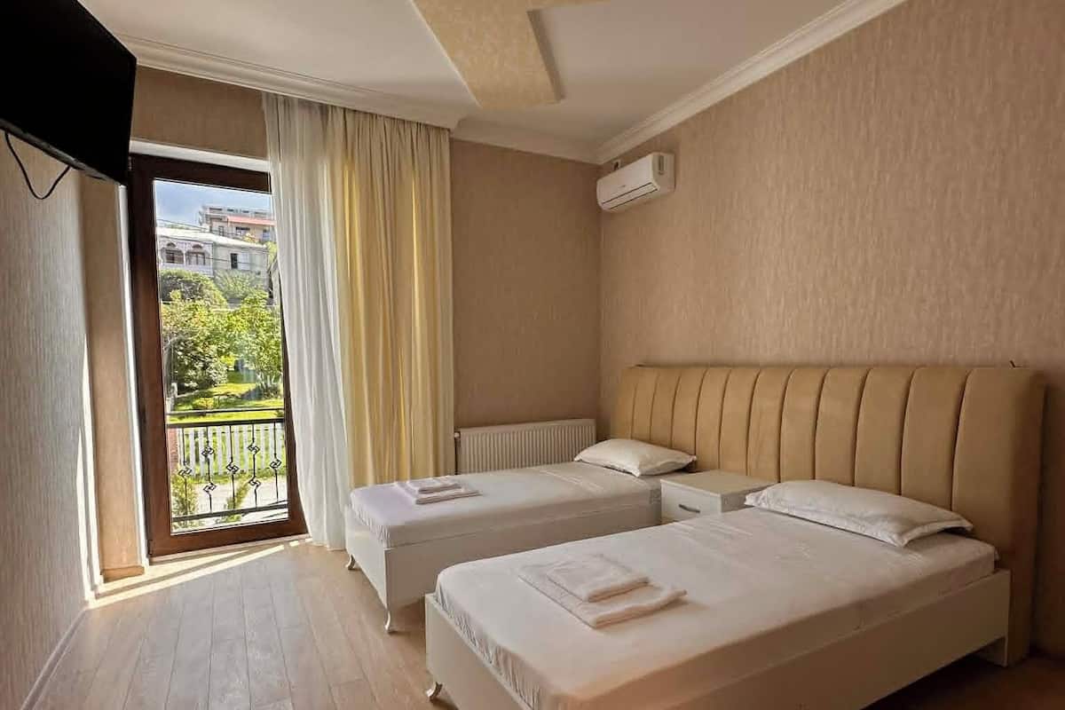 A hotel room with two beds, a ceiling light, an air conditioning unit, and a balcony with a view.