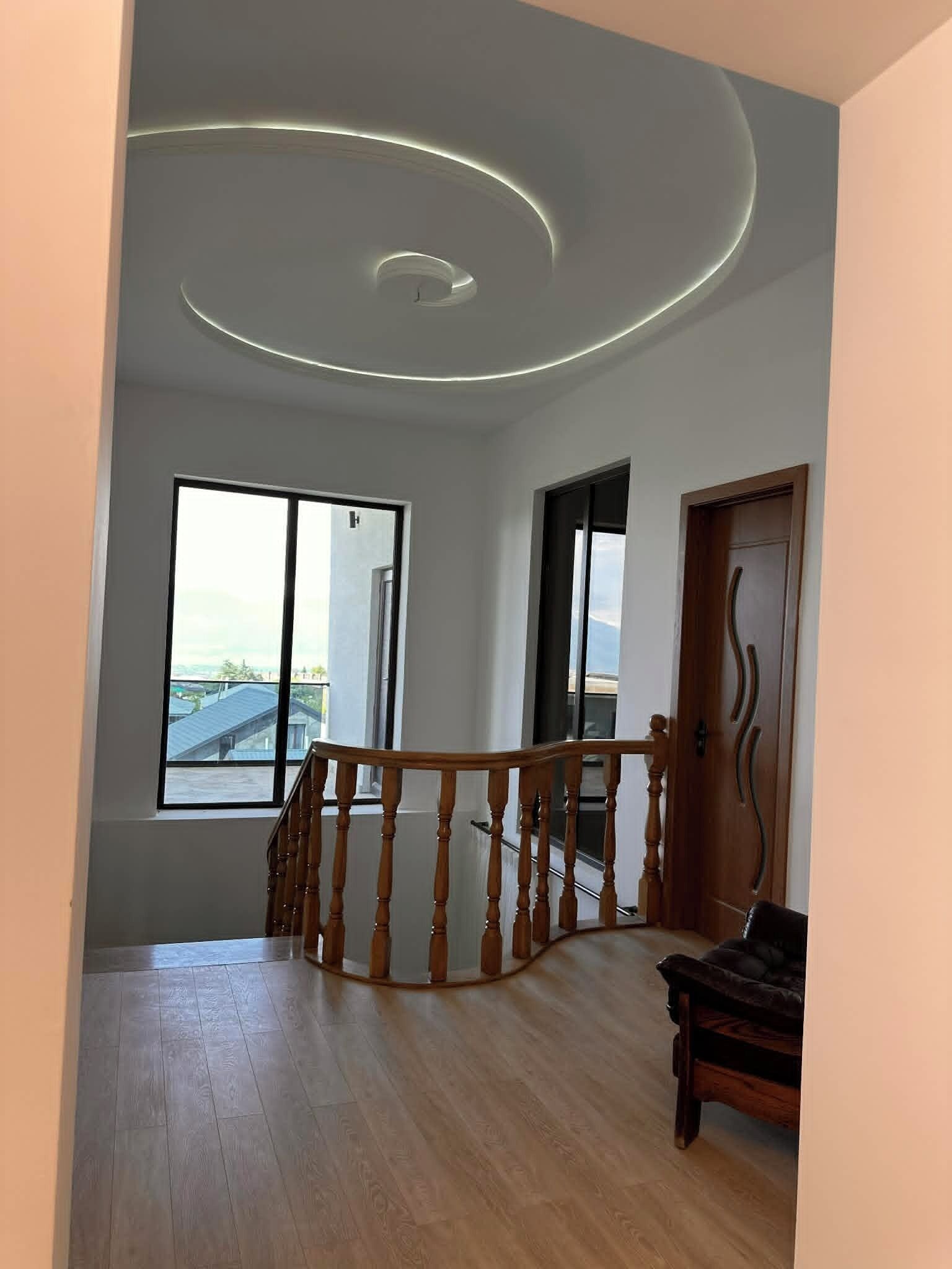 A spacious room with a wooden staircase, large windows, and a view of the outside.