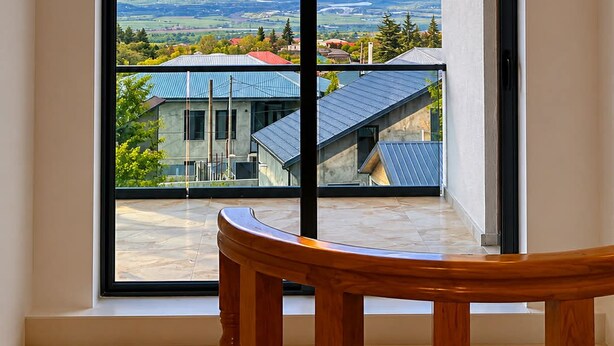Una habitación con un ventanal amplio, una silla de madera y vistas a montañas y casas.