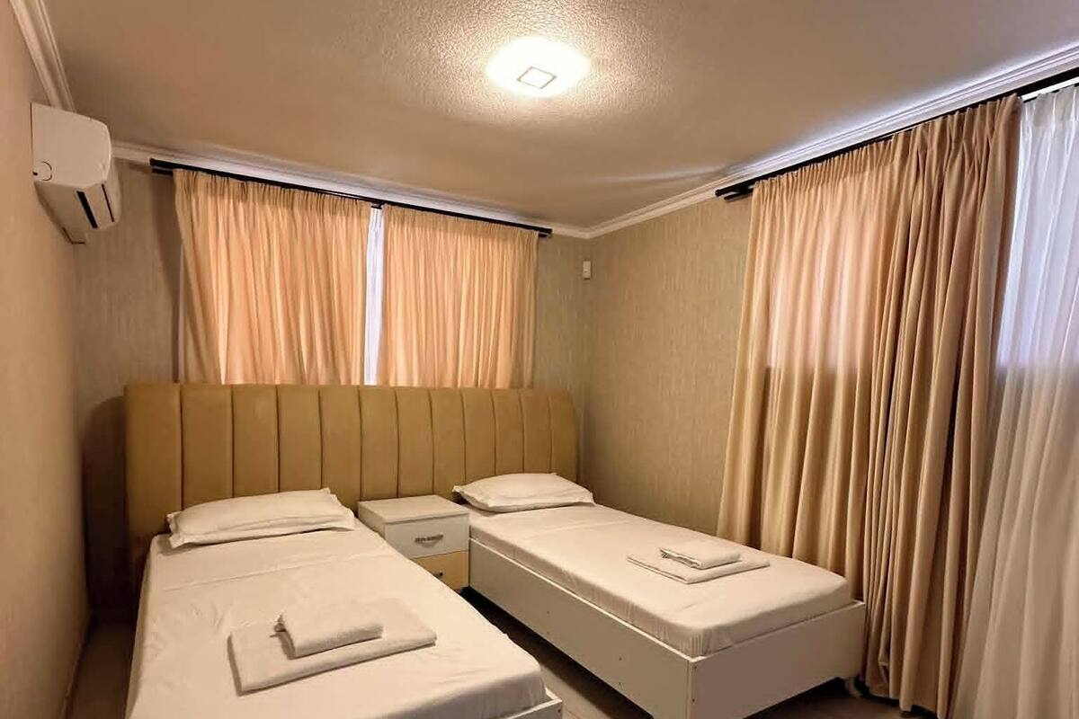 A room with two beds, a ceiling light, and curtains.