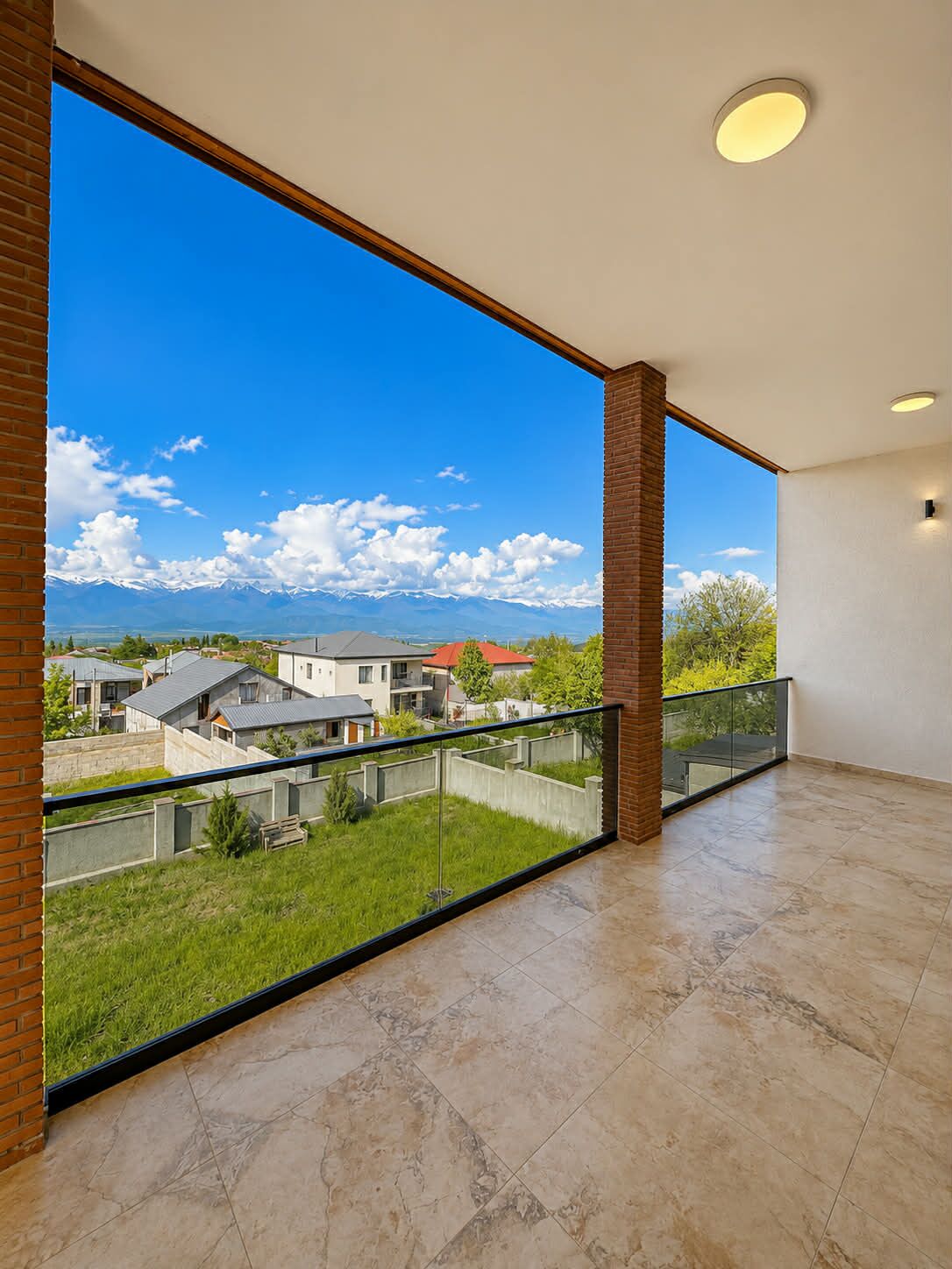 Un balcon spacieux offrant une vue dégagée sur un quartier résidentiel et les montagnes.