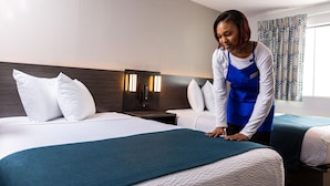 A hotel room with a bed, a nightstand, a lamp, and a window with curtains. - 2 Queen Beds|Suite,Nsmk, Sofa-Bed (Dallas)