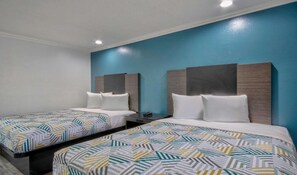Habitación de hotel con dos camas, una mesita de noche y una pared decorada en azul.