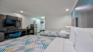 A hotel room with a bed, a desk with a TV, a chair, and a patterned rug.