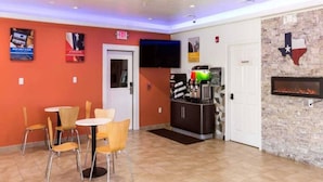 Un espace restaurant avec des tables et des chaises, une cuisine, un téléviseur et une cheminée ornée d’un drapeau du Texas.