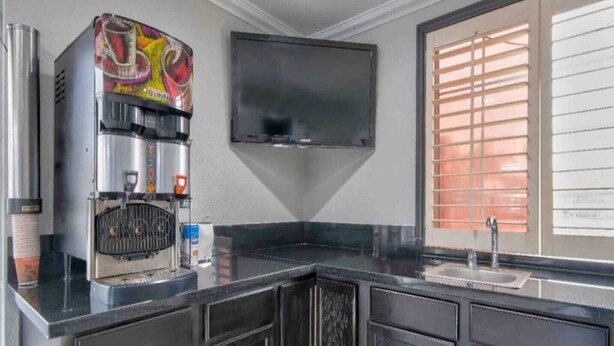 A kitchen with a coffee machine, a flat-screen TV, and a window with blinds.