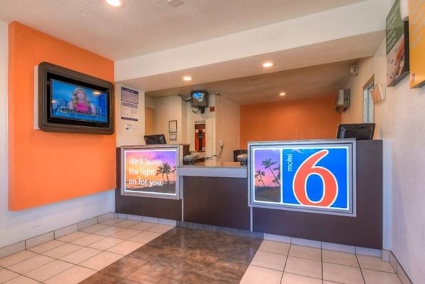 A hotel reception area with a TV screen, a digital display board, and a sign for room number 6.