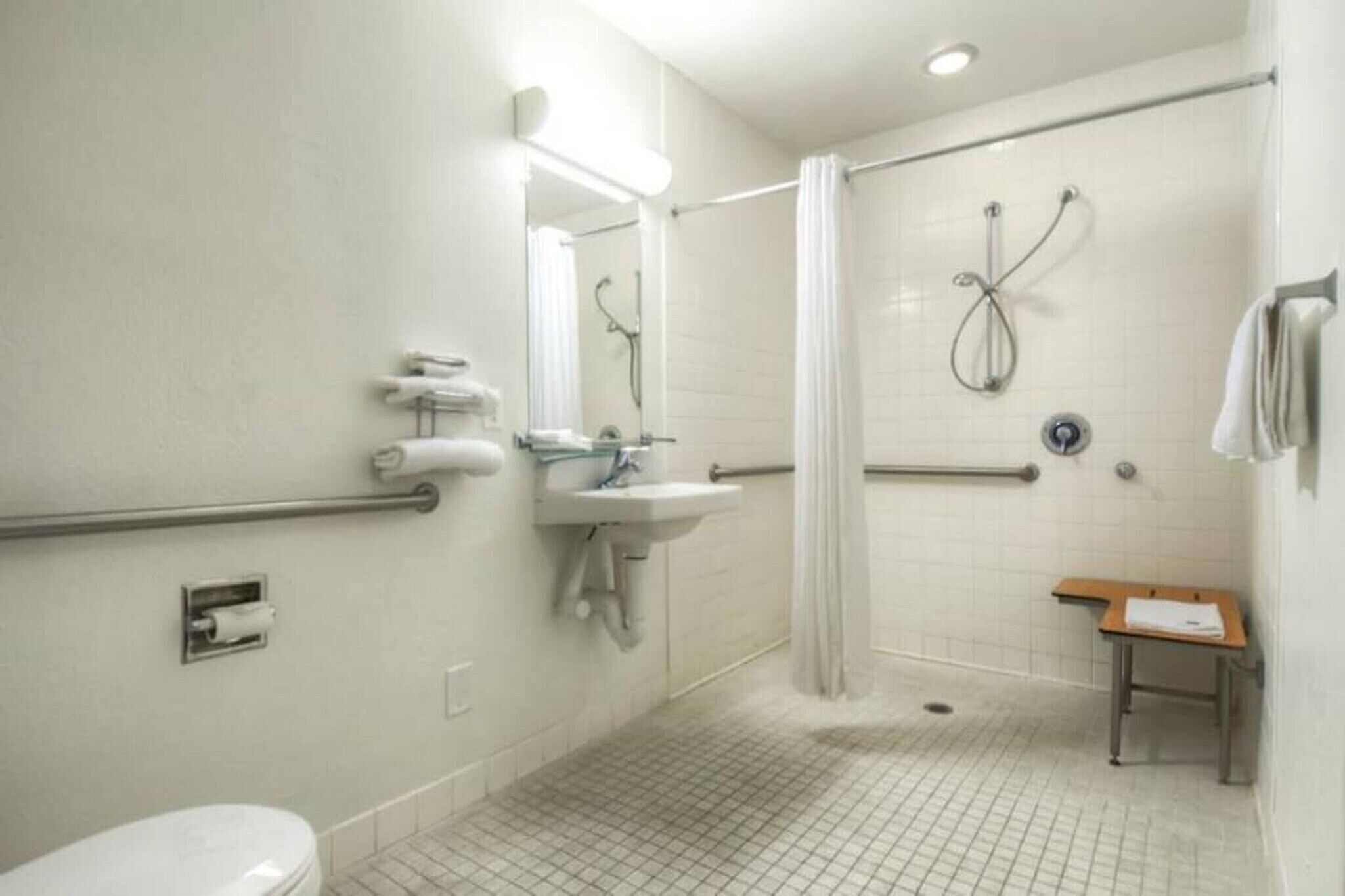 Baño estándar con inodoro, lavabo, ducha y una pequeña mesa con una toalla.