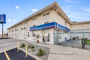 A motel with a 'WELCOME' sign, a fenced parking area, and a clear sky.