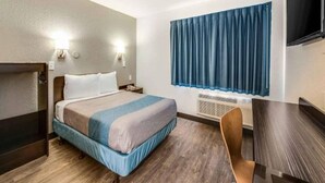 A hotel room with a bed, bedside table, lamp, window with curtains, and a TV. - 1 King Bed | Mob Access Tub Nsmk Minifridg (Fort Wayne)