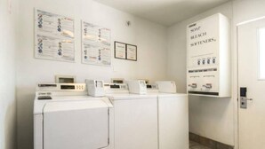 A laundry area with multiple washing machines, a wall-mounted information board, and a door with a sign. - 1 King Bed | Mob Access Tub Nsmk Minifridg (Fort Wayne)