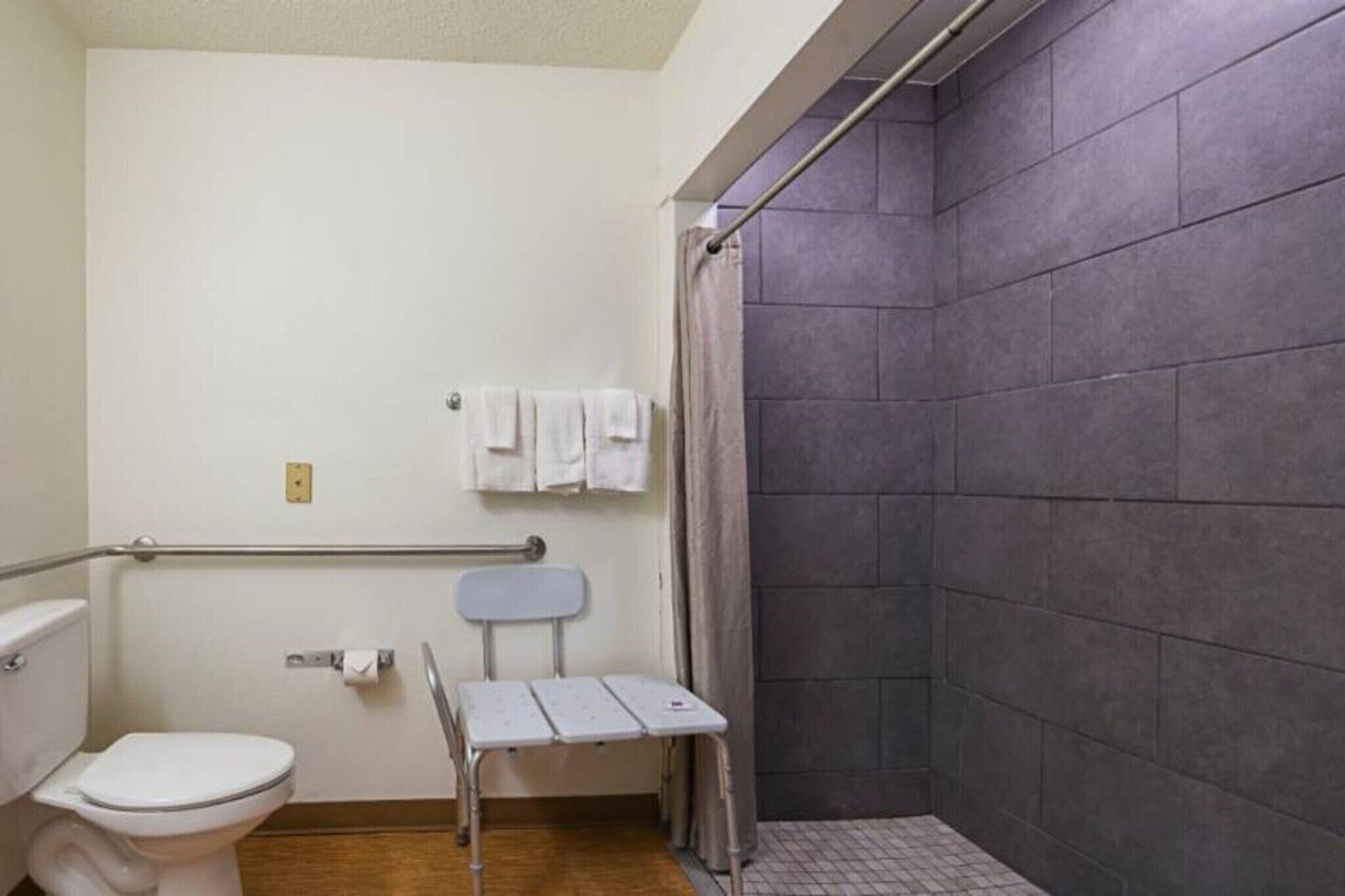 A bathroom with a white toilet, a shower with a grey curtain, and a small white bench.