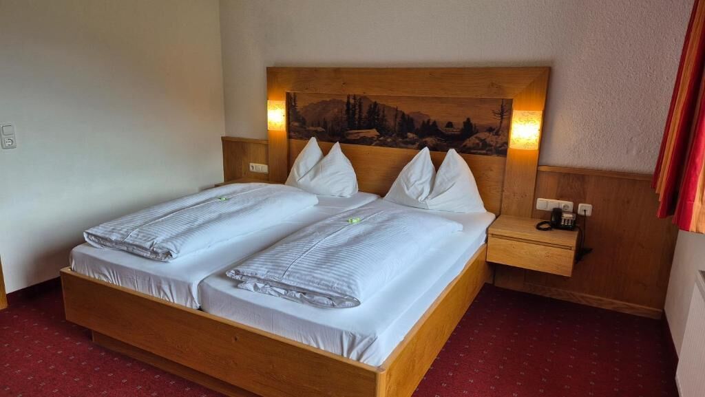 A double bed with a wooden headboard, two bedside tables, and a wall-mounted lamp.