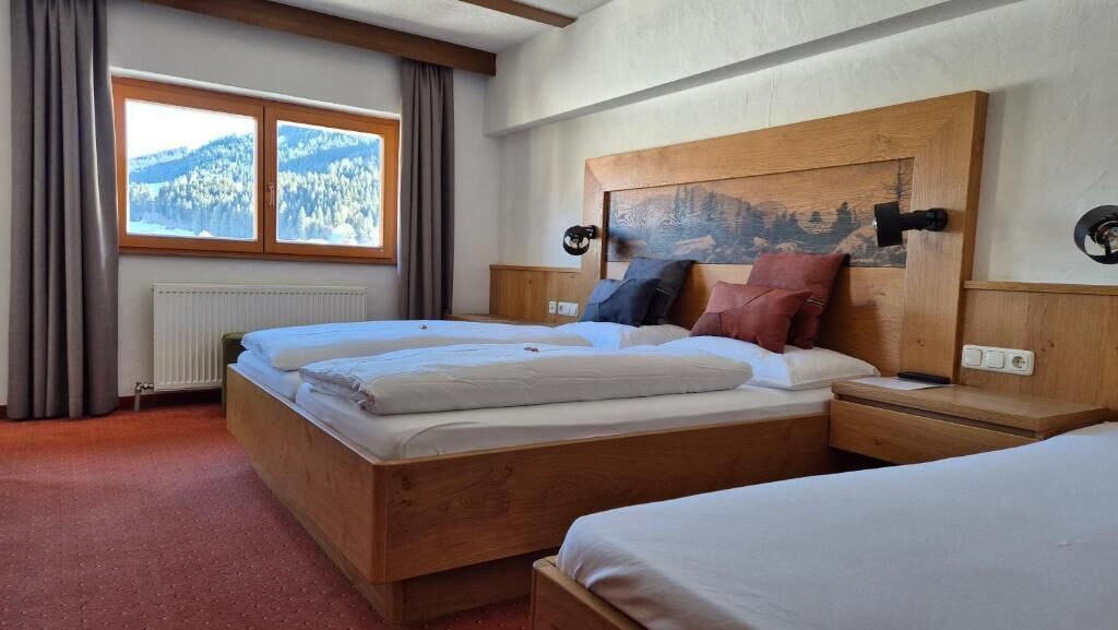 A hotel room with a wooden bed, a nightstand, a window with a view of mountains, and a radiator.