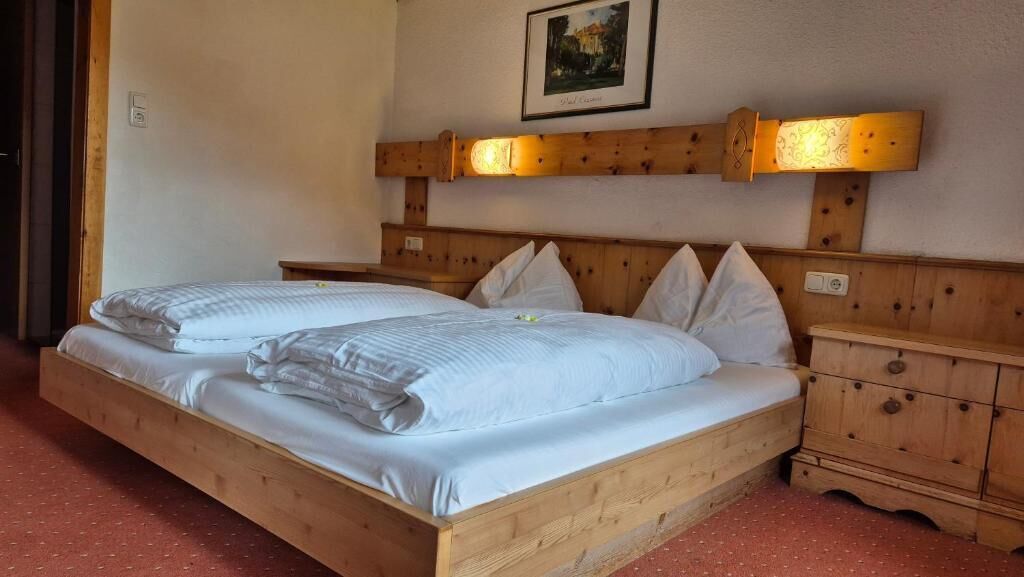 A wooden bed with two pillows, a wooden nightstand, and a wall-mounted lamp.