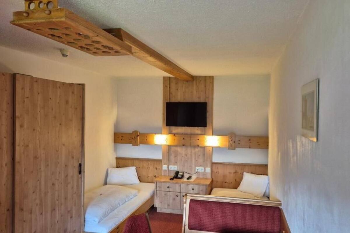 Habitación de hotel con dos camas, un televisor montado en la pared y un techo de madera.