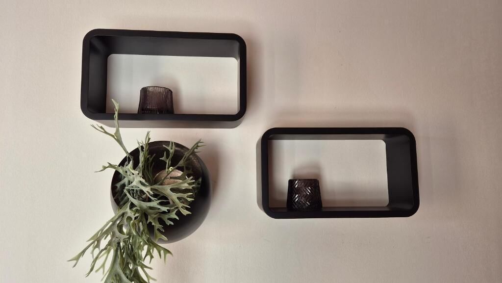 Three black-framed mirrors on a wall, with a potted plant to the left.