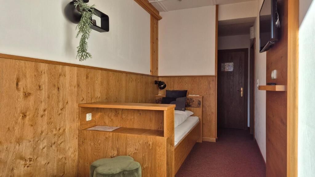Ein Zimmer mit einem hölzernen Etagenbett, einem Schreibtisch, einem Stuhl, einem kleinen Hocker, einem Fernseher und einer Pflanze.