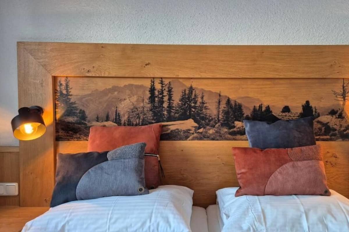 Una cama doble con cabecera de madera, dos mesitas de noche y dos lámparas fijadas a la pared.