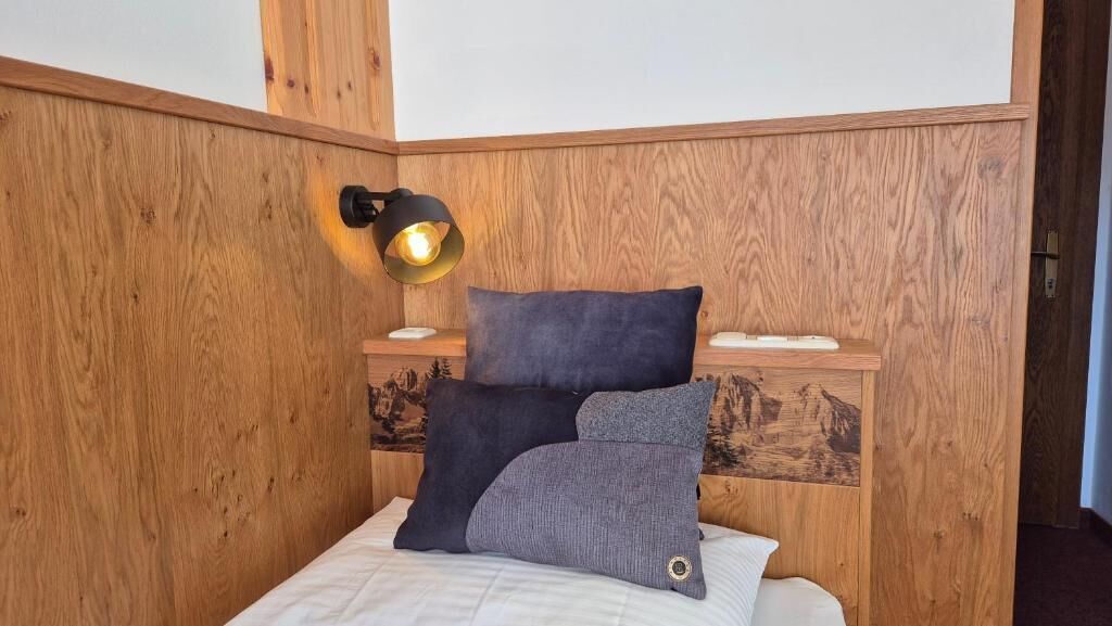 A wooden headboard with a wall-mounted lamp, two pillows, and a bedside table with a small decorative item.