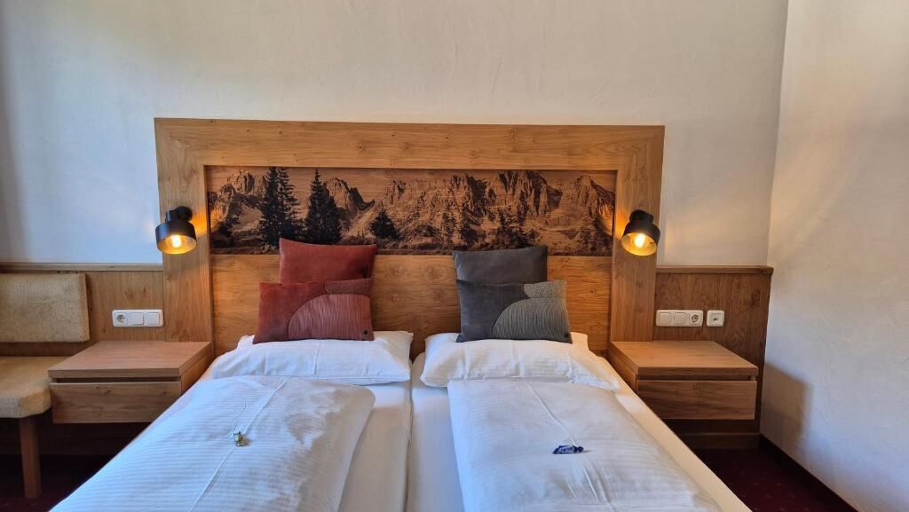 Un lit double avec une tête de lit en bois, deux tables de chevet et une lampe fixée au mur.