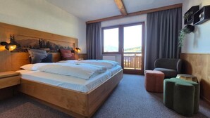 A room with a large bed, a chair, a small table, and a view of the outdoors. - Hotel Dahoam by Miha (Westendorf)