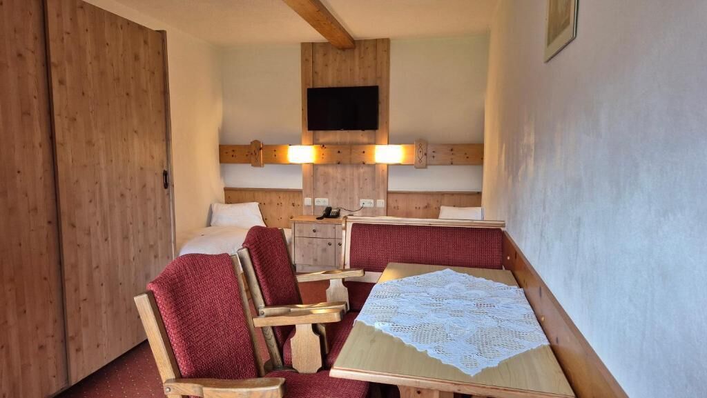 A room with a wooden headboard, a television mounted above the bed, a small bedside table, and a table with a lace tablecloth.