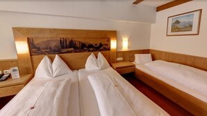 A hotel room with two beds, a wooden headboard, a painting, and a nightstand with a phone. - Hotel Dahoam by Miha (Westendorf)