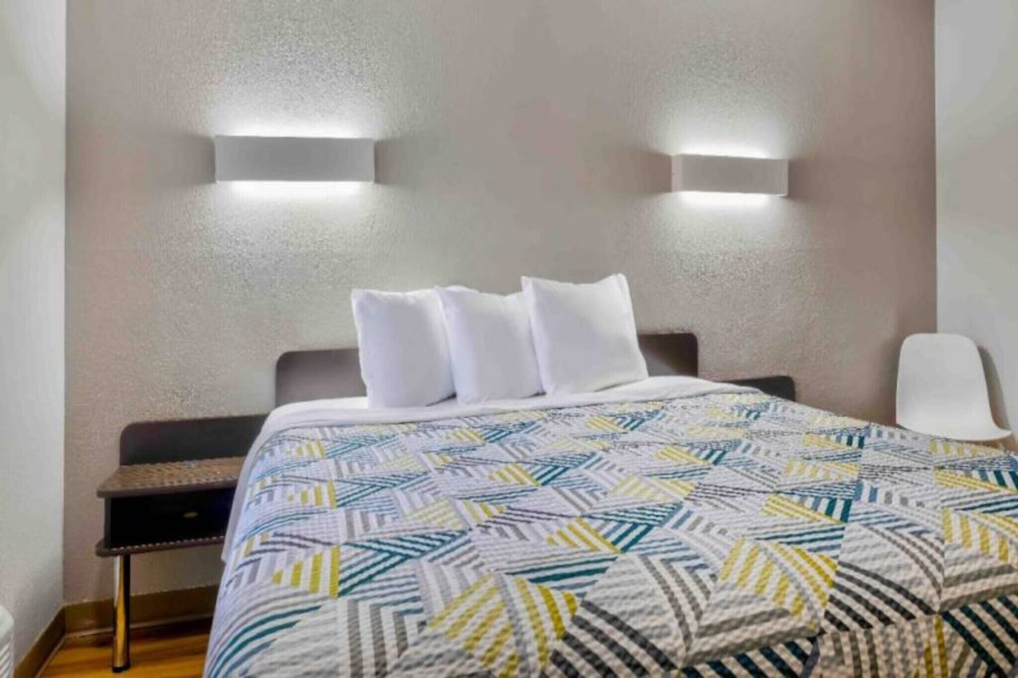 A bedroom with a bed, pillows, a bedside table, and wall-mounted lights.