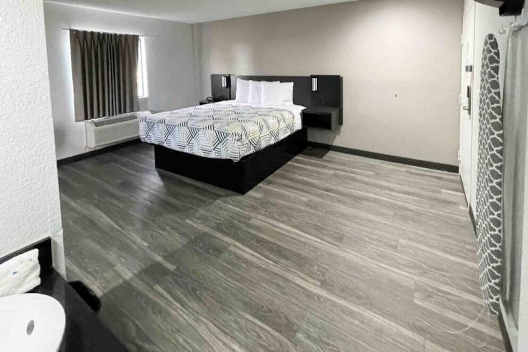 Une chambre à coucher comprenant un lit, une table de chevet, un radiateur fixé au mur et une fenêtre avec des rideaux.