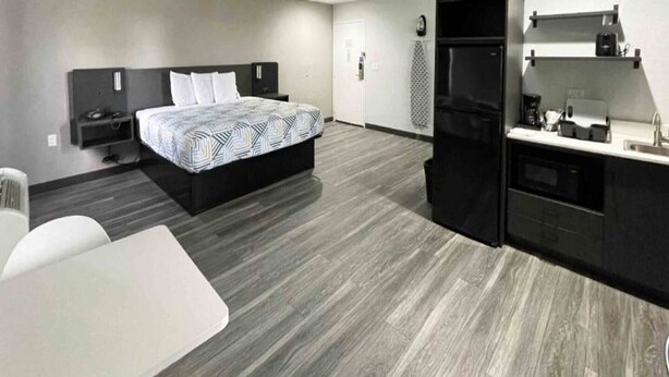 Ein modernes Hotelzimmer mit Bett, einer kleinen Küchenzeile, einem weißen Tisch und einem grauen Boden.