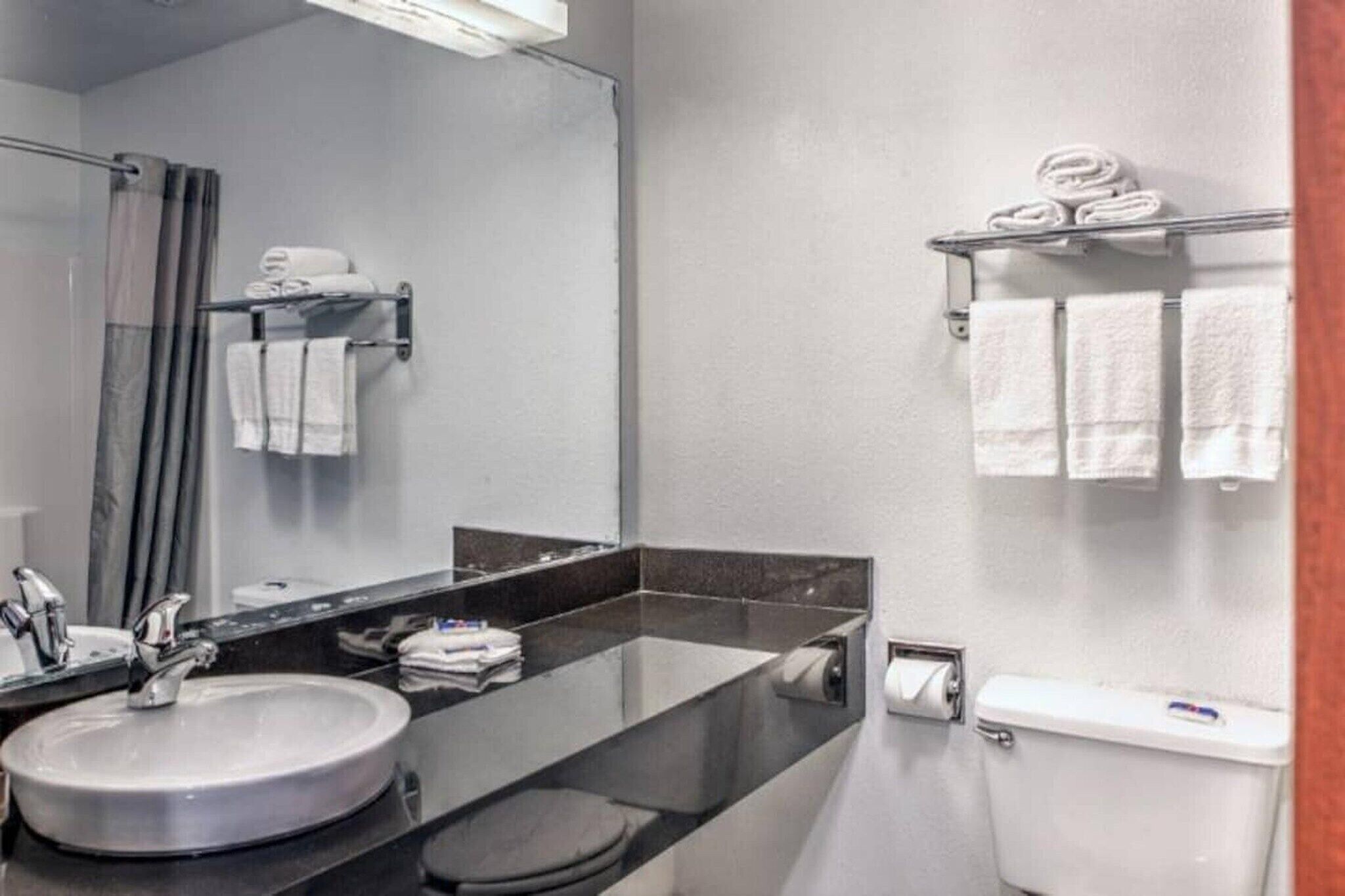A modern bathroom with a sink, mirror, toilet, and towel rack.