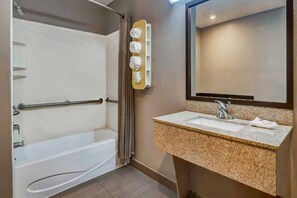 A bathroom with a bathtub, a sink with a granite countertop, a towel rack, and a mirror.